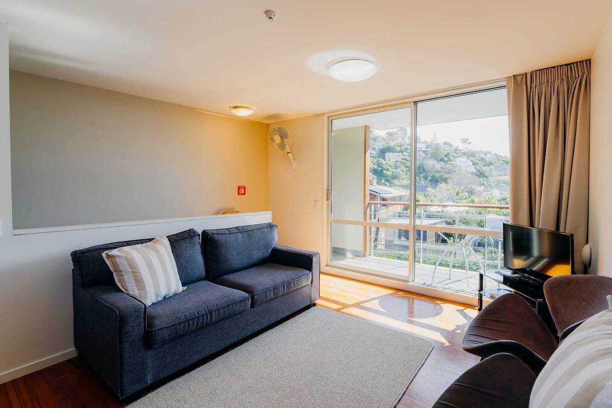 A modern living room with a sofa, a TV, and a large sliding glass door leading to a balcony.