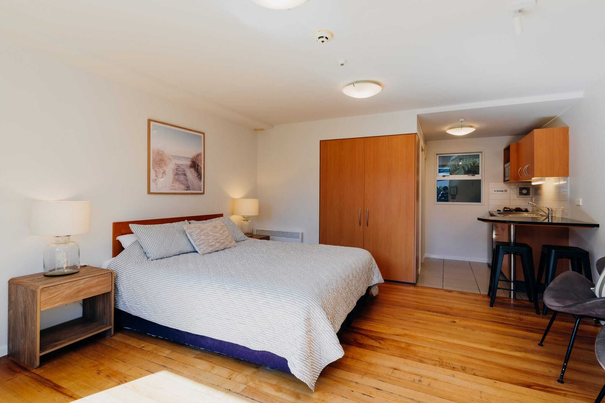 A bedroom with a wooden bed, bedside tables, a desk, and a chair.