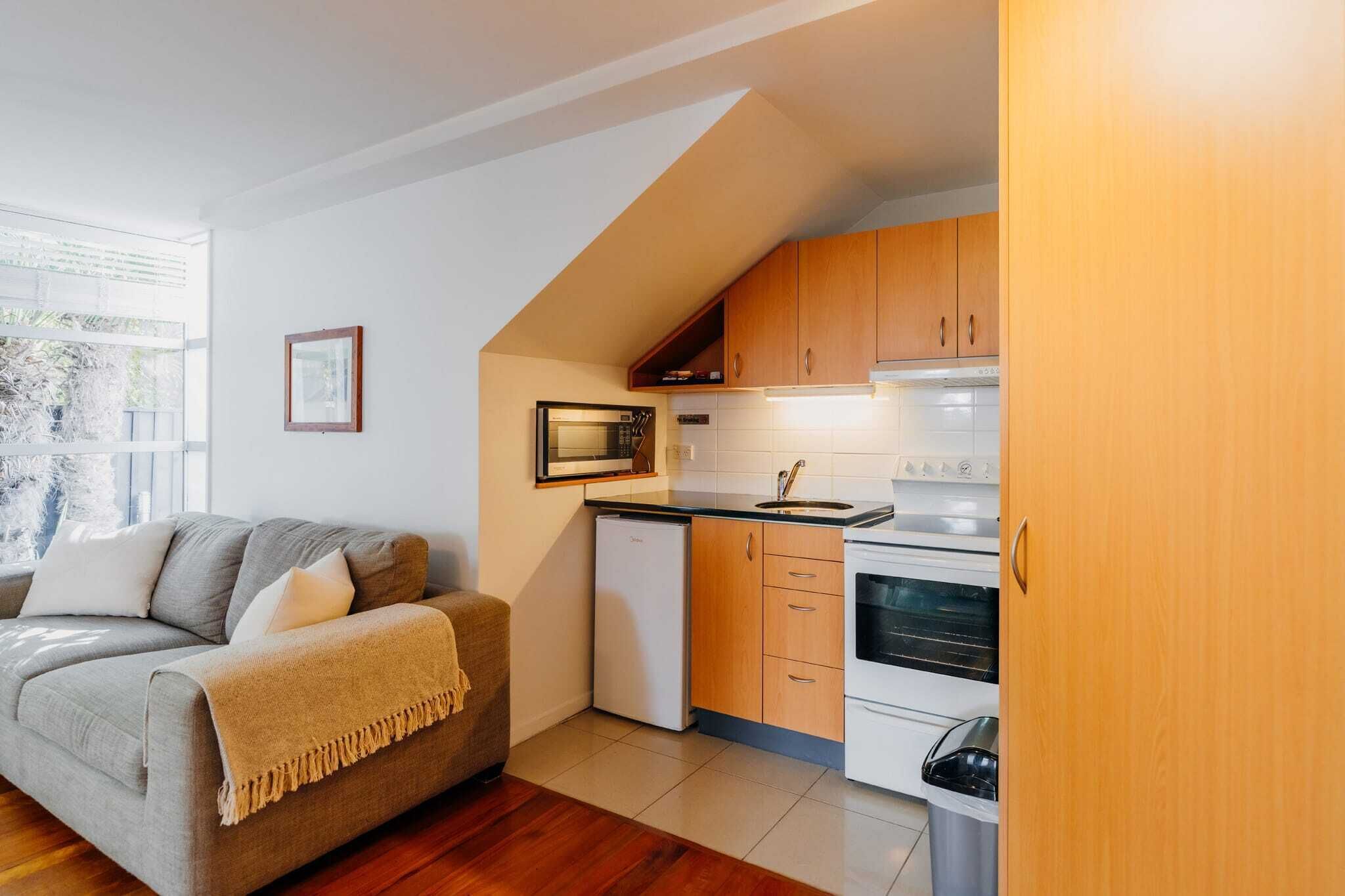 Una cocina compacta con muebles de madera, un microondas, un refrigerador pequeño y una estufa.