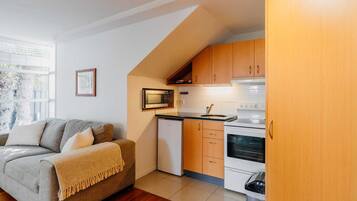 Una cocina compacta con muebles de madera, un microondas, un refrigerador pequeño y una estufa.