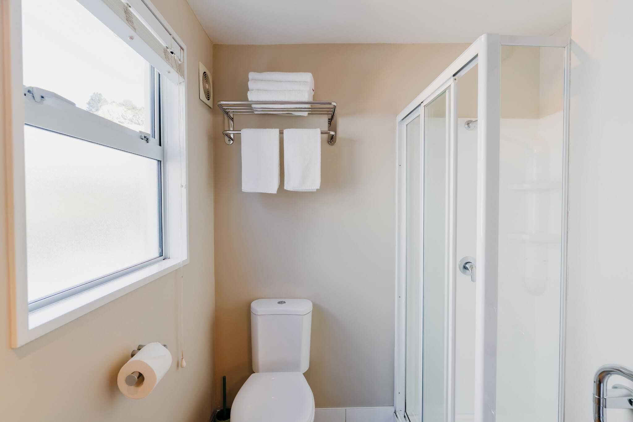 Un baño con inodoro, toallero con toallas, zona de ducha y ventana.