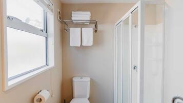 Un baño con inodoro, toallero con toallas, zona de ducha y ventana.