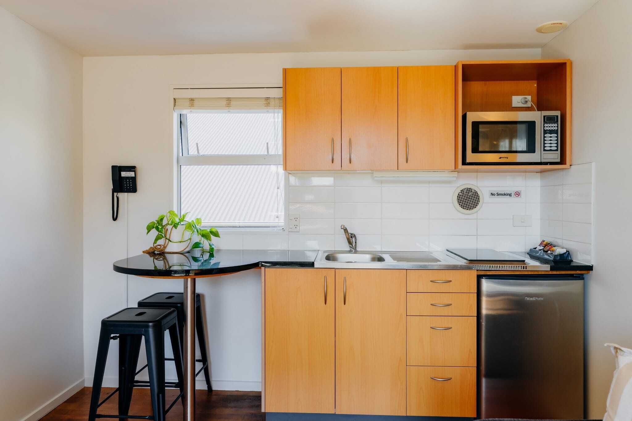 A compact kitchen with wooden cabinets, a microwave, a sink, and a refrigerator.
