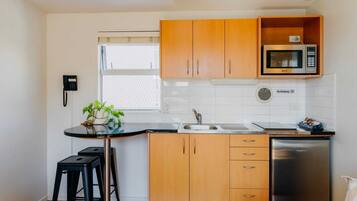 A compact kitchen with wooden cabinets, a microwave, a sink, and a refrigerator.