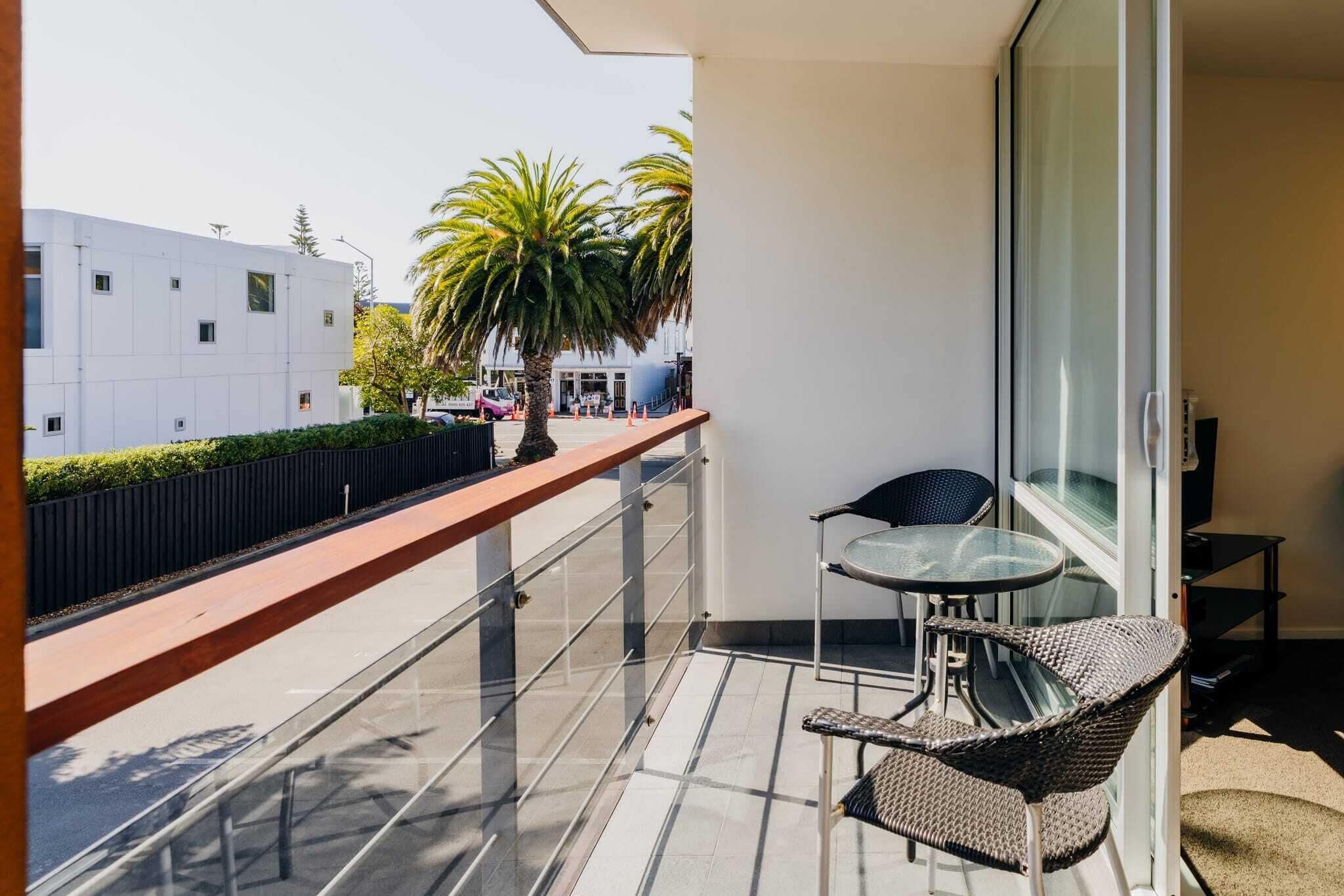 Un balcon doté d’une balustrade en verre, de deux fauteuils en osier et d’une petite table.