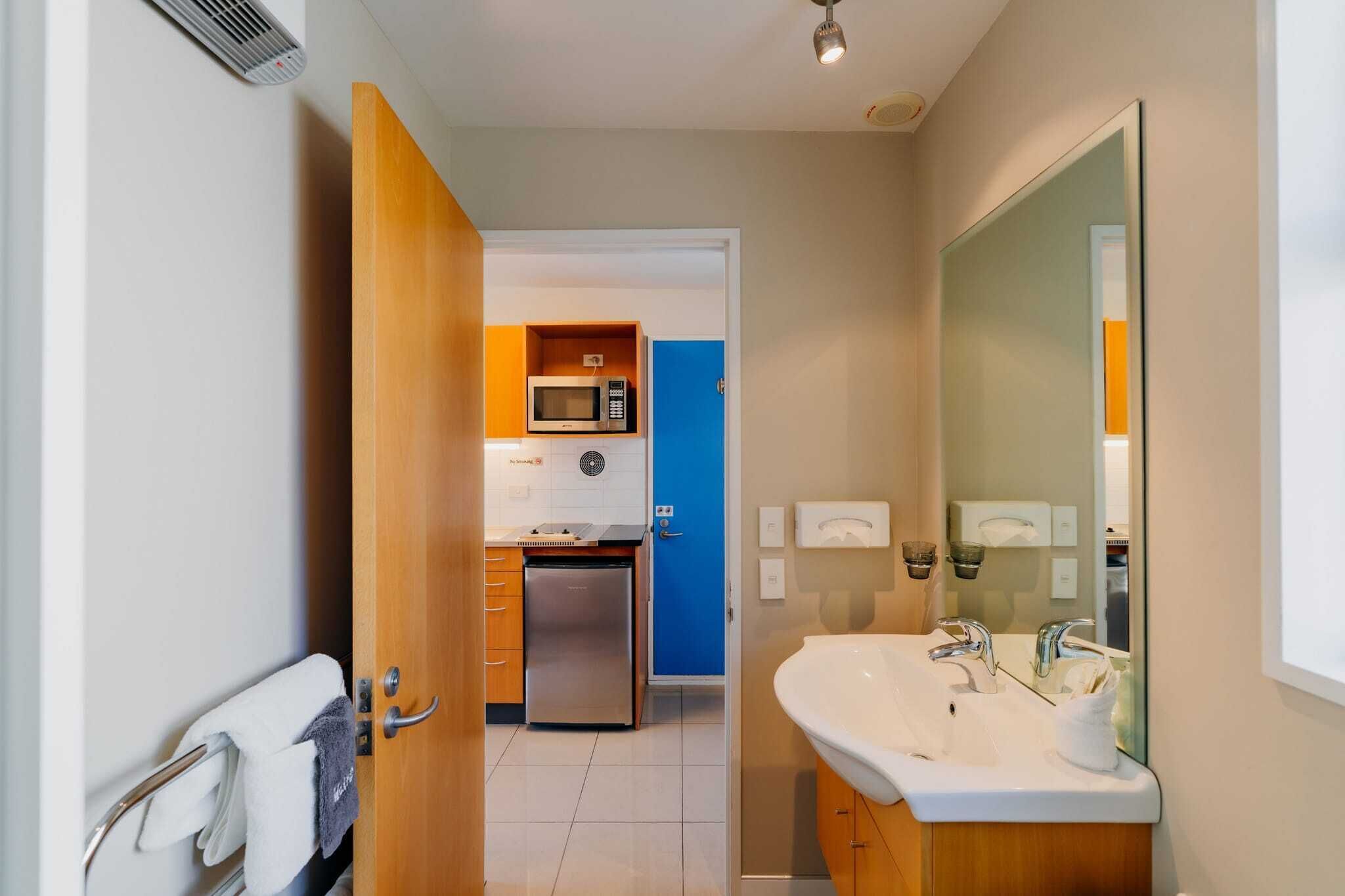 Habitació d'hotel petita amb zona de cuina, un rentapeus i un mirall.
