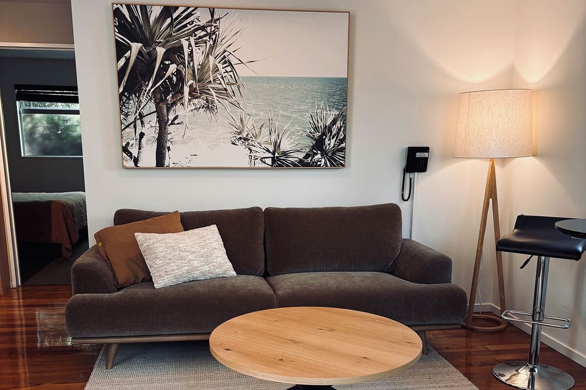 A modern living room with a sofa, a round coffee table, a floor lamp, and a painting of a beach scene.