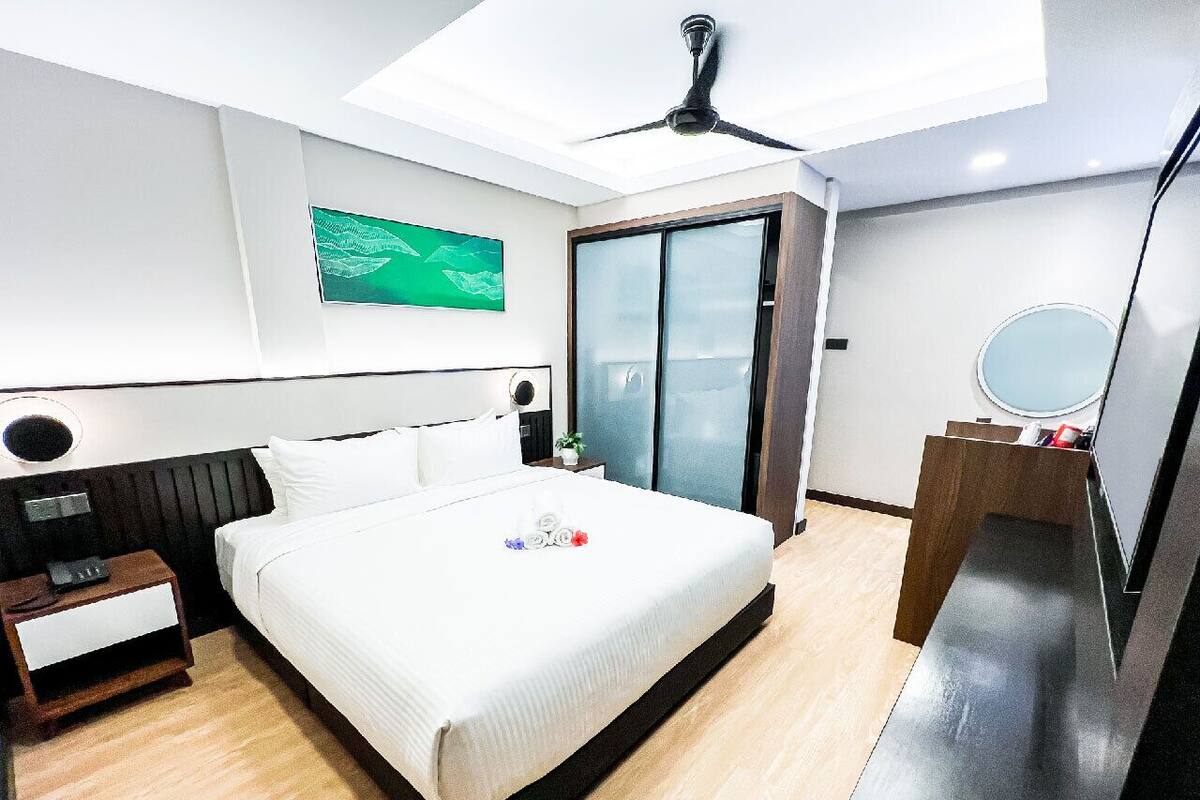 A modern hotel room with a large bed, a ceiling fan, a small desk, a mirror, and a sliding glass door.