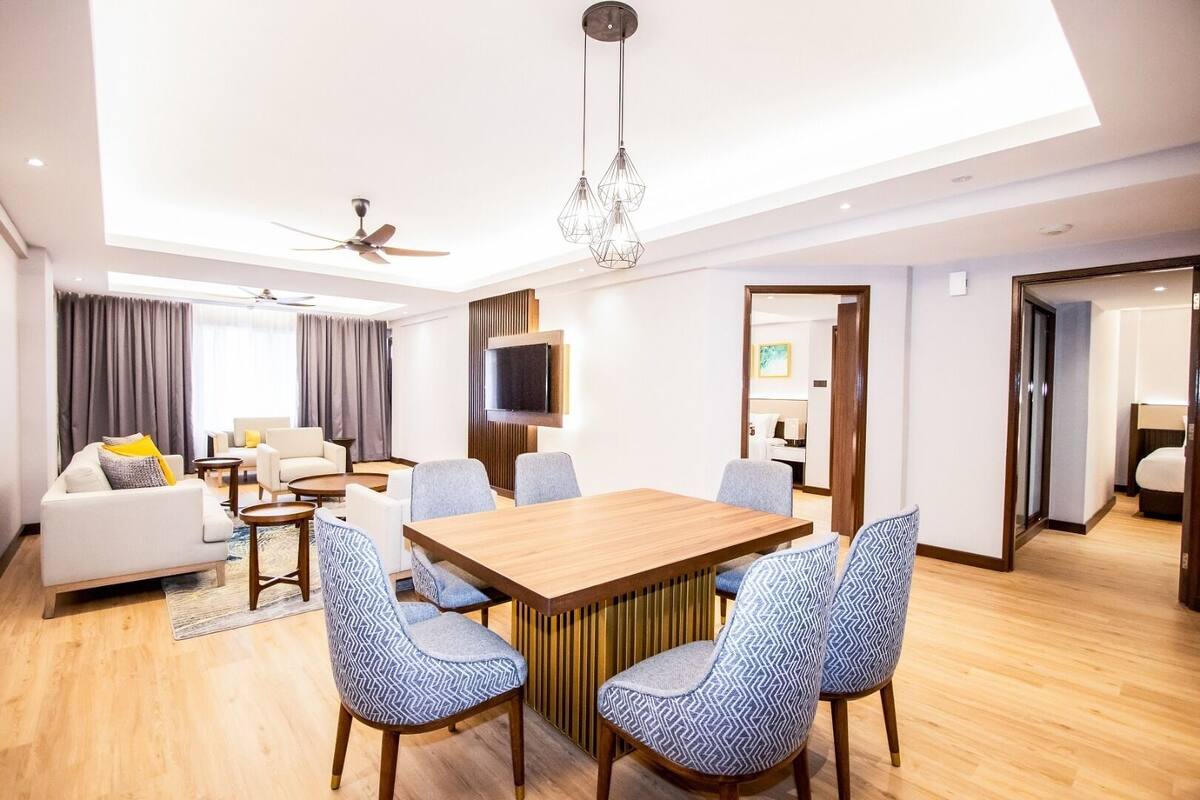 A modern hotel room with a dining area, a sofa, a TV, and a ceiling fan.