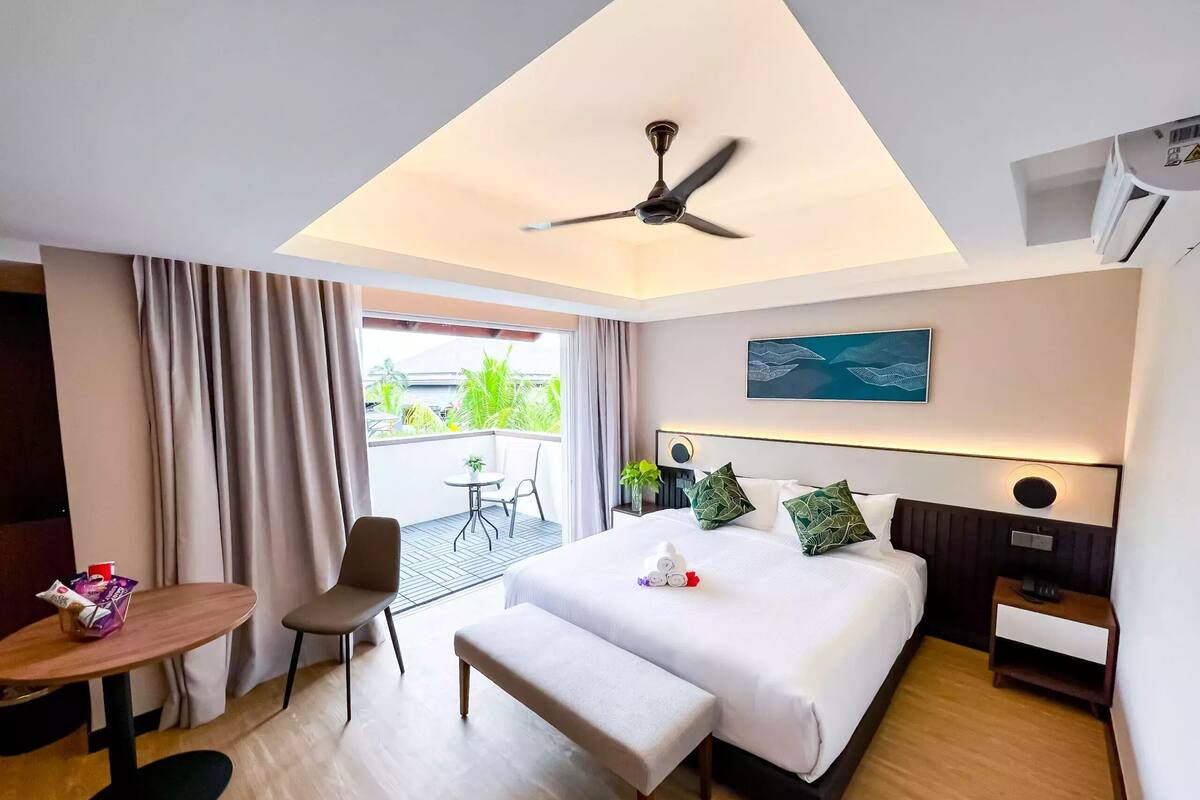 A hotel room with a bed, bedside table, chair, and a small balcony with a table and chair.