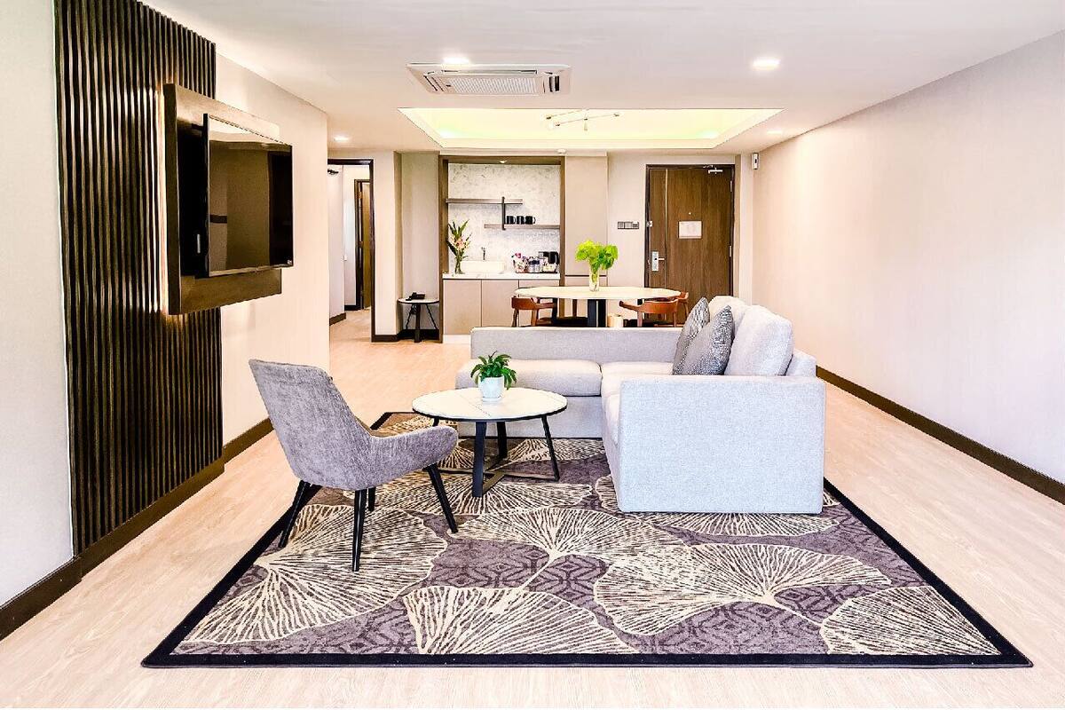 A modern living room with a sofa, two armchairs, a coffee table, and a TV mounted on the wall.
