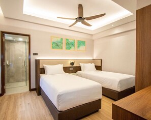 Habitación de hotel con dos camas, ventilador de techo, cabina de ducha de vidrio y tres obras de arte colgadas en la pared.