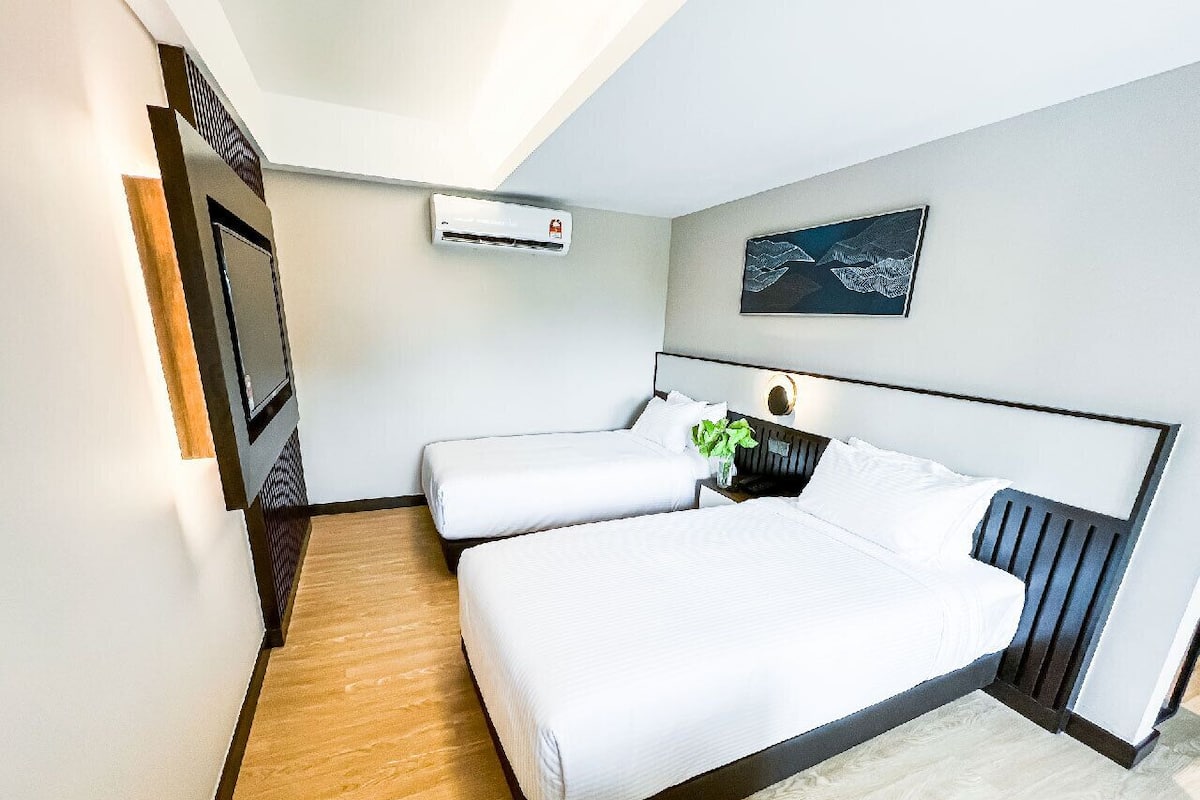 A modern hotel room with a large bed, a small bedside table, an air conditioning unit, and a framed artwork on the wall.