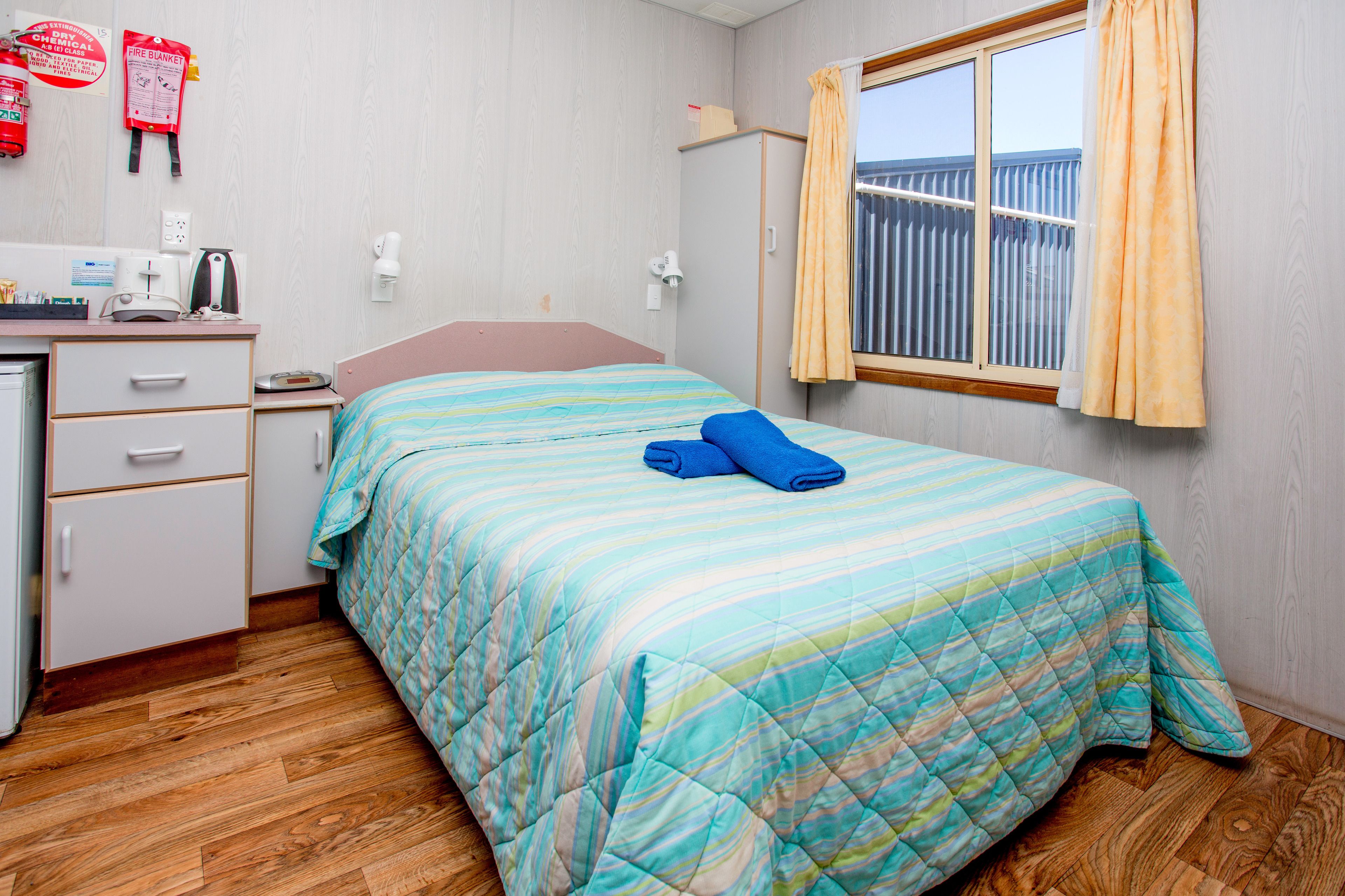 A bedroom with a bed, a desk, a wardrobe, and a window with curtains.