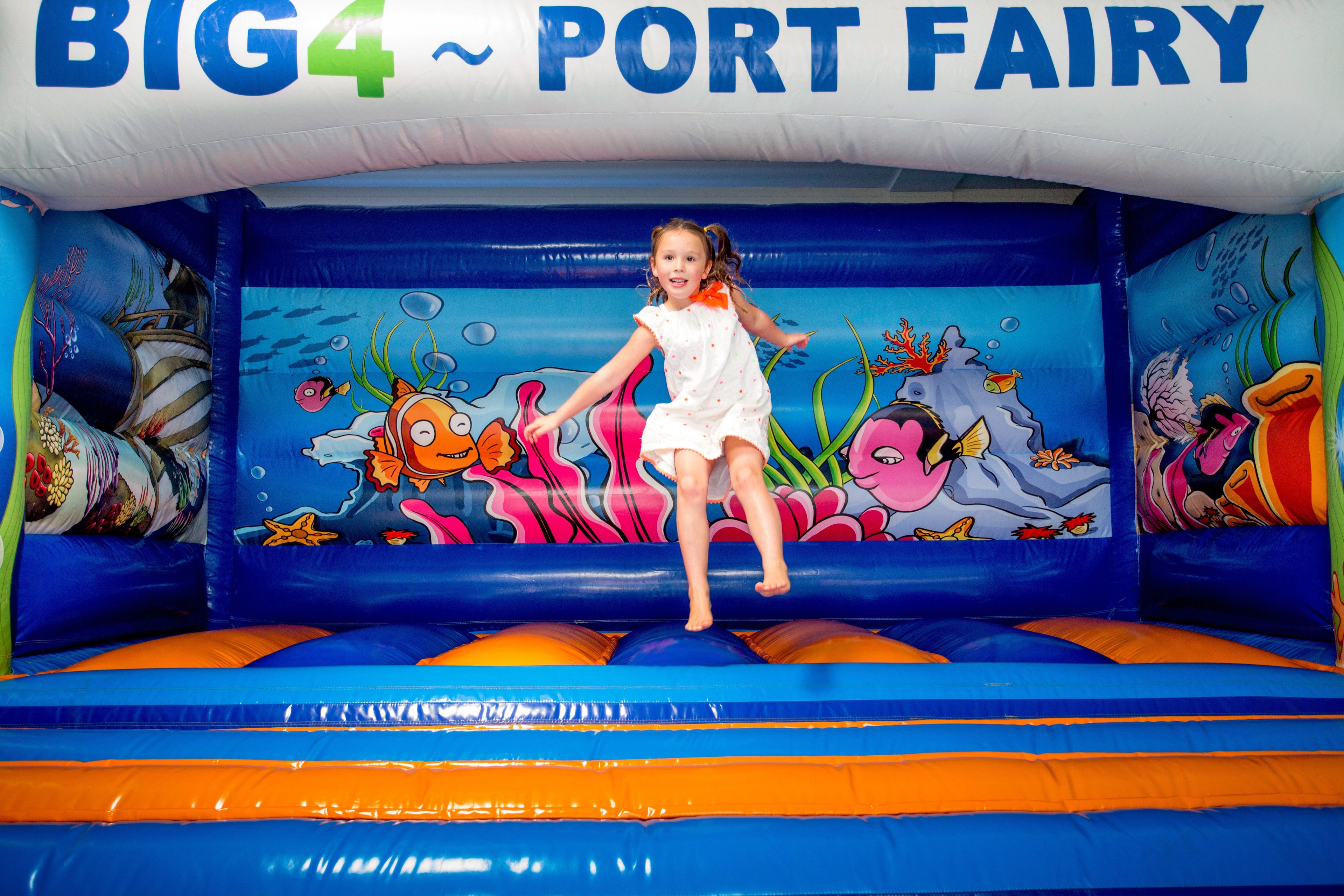 A child jumping on a colorful inflatable play area with a marine-themed mural.