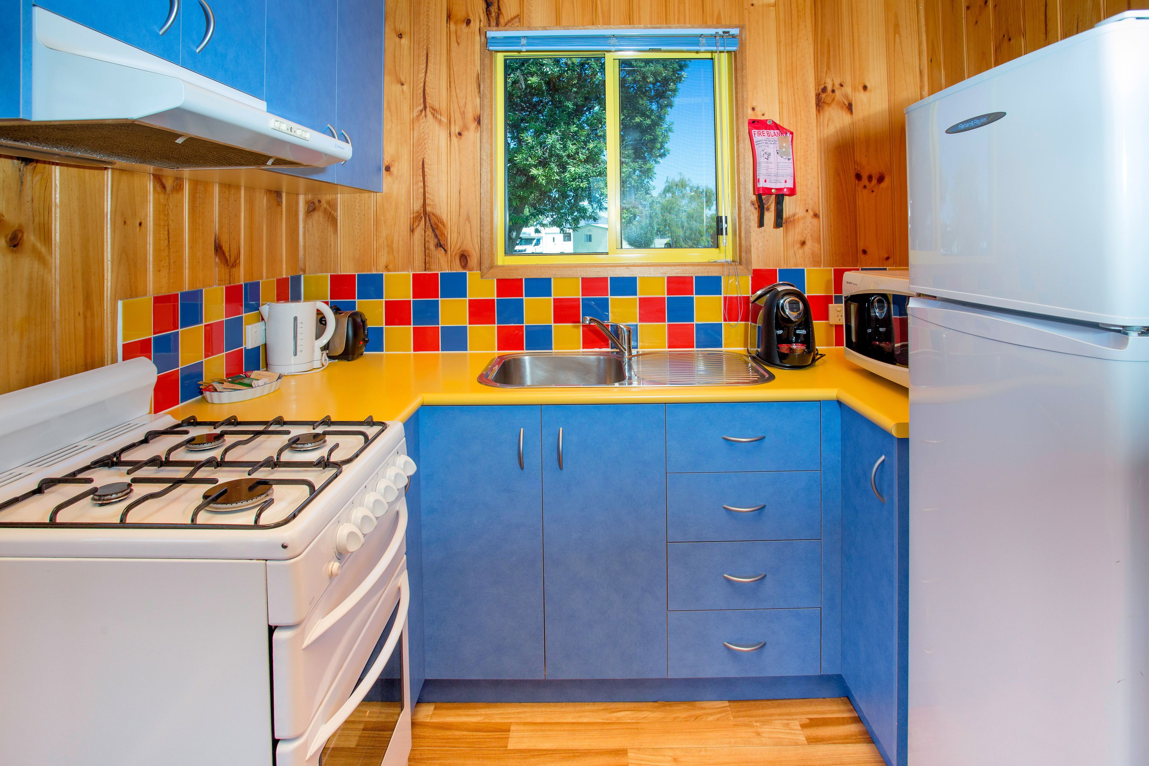 A compact kitchen with a gas stove, a white refrigerator, and a window with a view of trees.