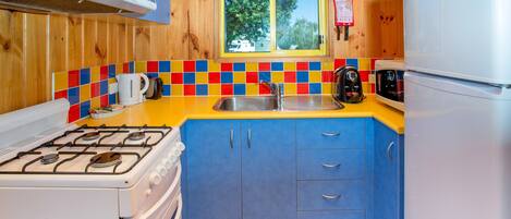 A compact kitchen with a gas stove, a white refrigerator, and a window with a view of trees.