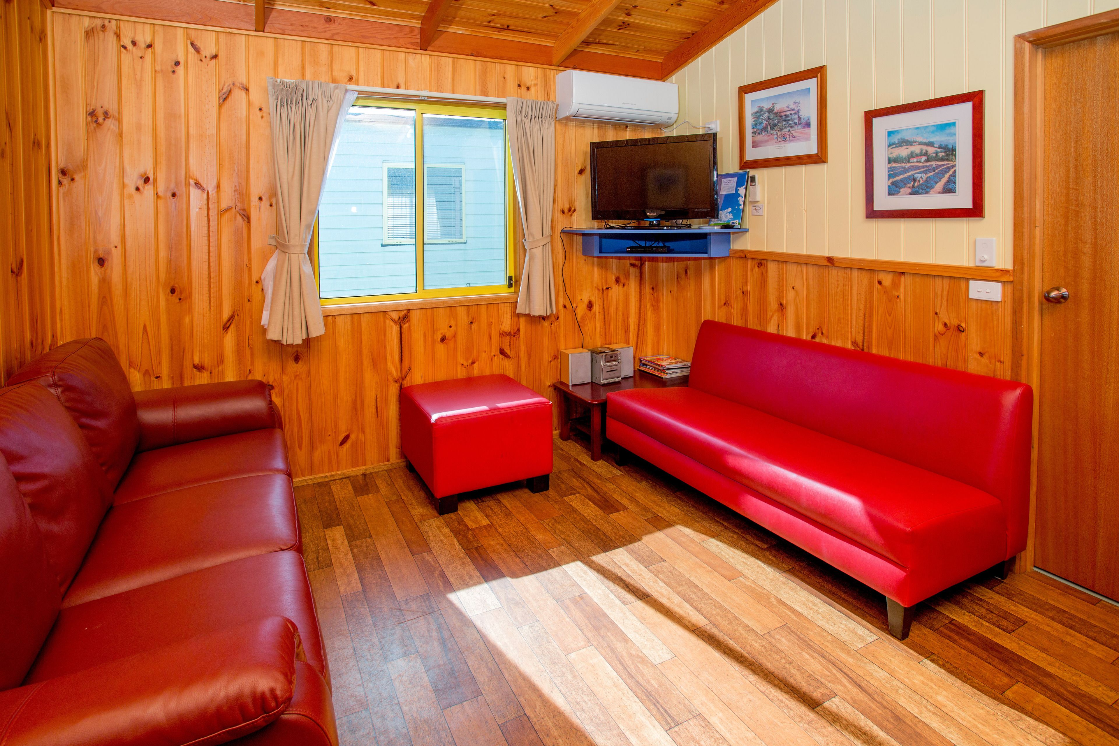 Ein Zimmer mit Holzwänden, einer roten Ledersofa, einem roten Hocker, einem Fernseher und gerahmten Bildern an der Wand.