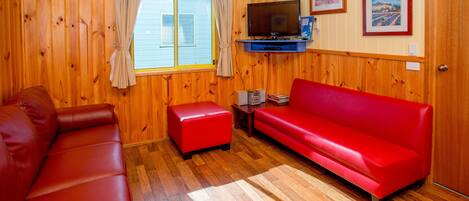 Ein Zimmer mit Holzwänden, einer roten Ledersofa, einem roten Hocker, einem Fernseher und gerahmten Bildern an der Wand.