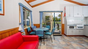 A compact kitchen with a microwave and oven, a dining area with a table and chairs, and a red sofa. - BIG4 Port Fairy (Port Fairy)