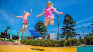 Two individuals jumping on a trampoline in an outdoor area with a blue sky, trees, and a fence. - BIG4 Port Fairy (Port Fairy)