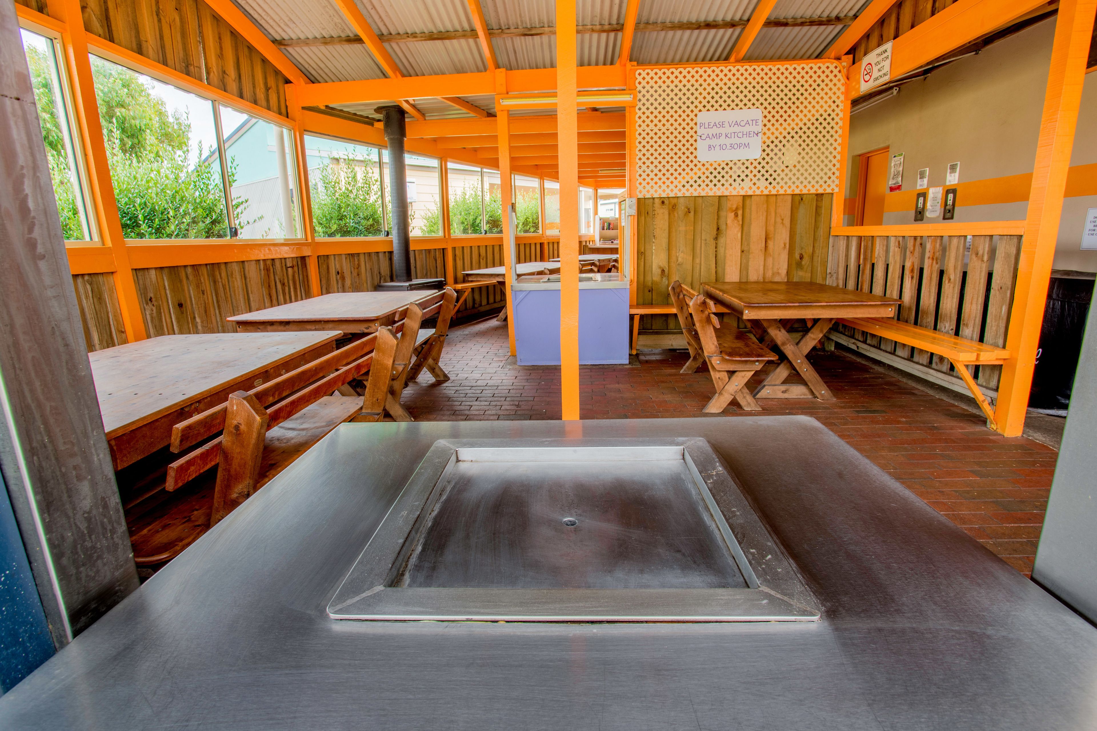 A rustic wooden interior with tables and benches, a central sink, and a sign indicating a kitchen area.
