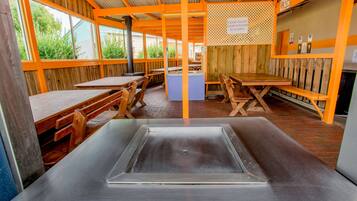 A rustic wooden interior with tables and benches, a central sink, and a sign indicating a kitchen area.