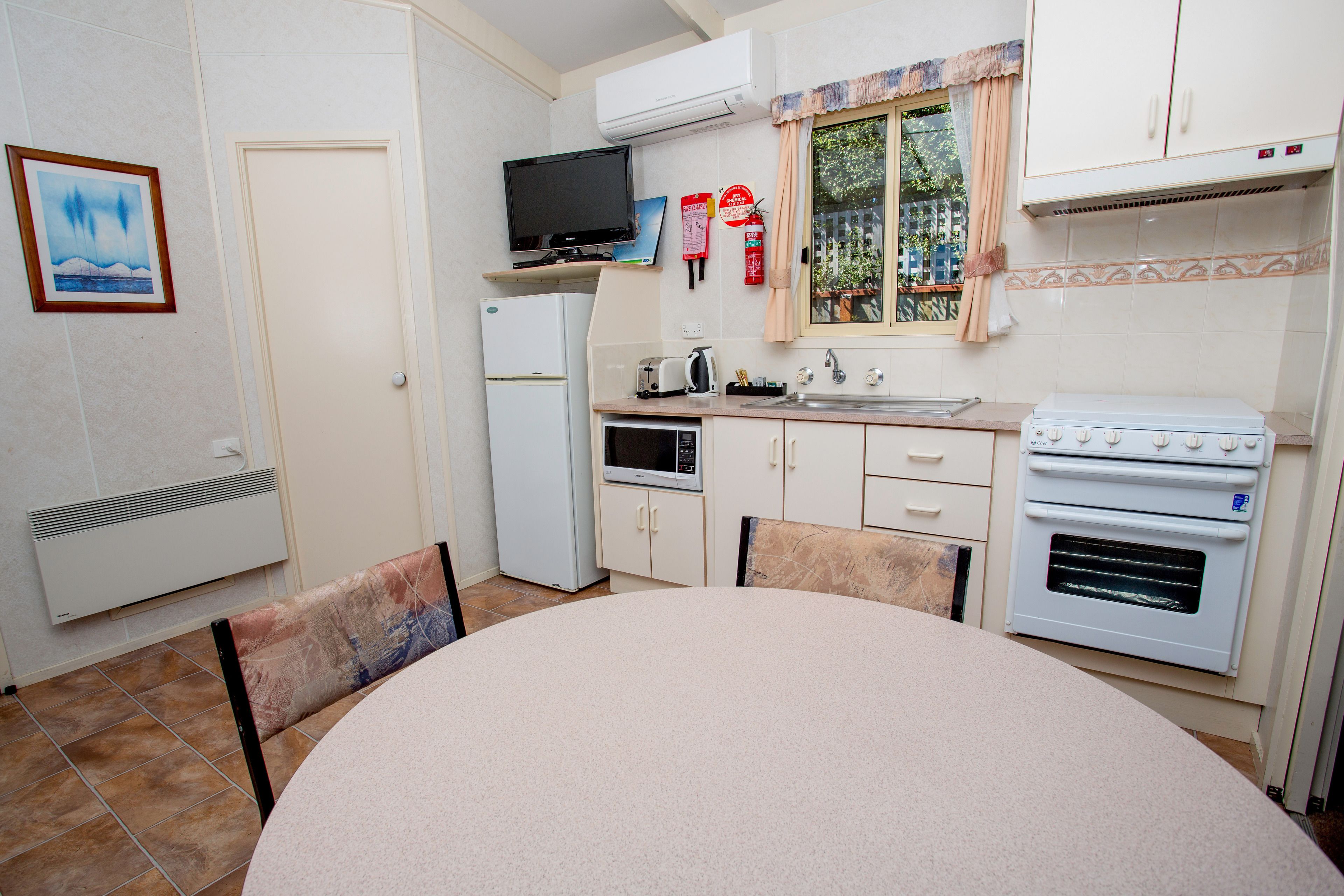 A compact kitchen with a refrigerator, microwave, stove, and a television on a shelf.