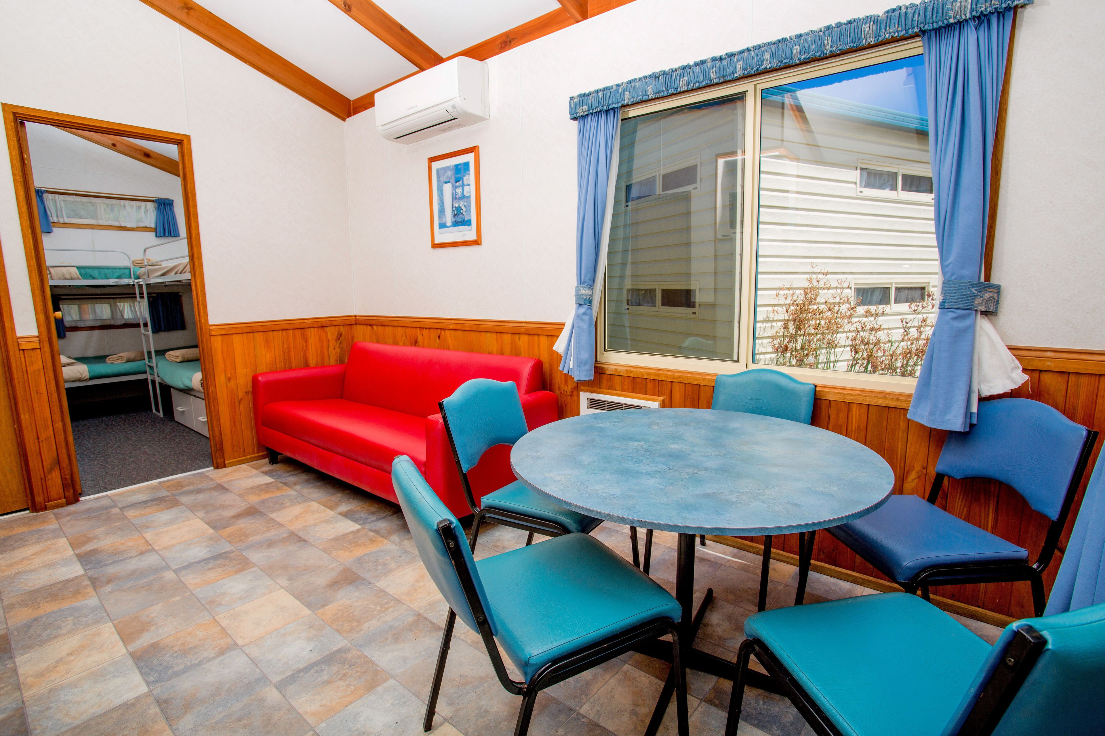 A room with a red sofa, blue chairs, a round table, and a large window with curtains.