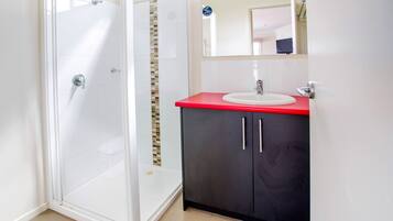 Ein Badezimmer mit Duschkabine aus Glas, einem weißen Waschbecken mit roter Arbeitsplatte und einem dunklen Schrank mit silberfarbenen Griffen.