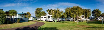 Un parque para caravanas con varias caravanas estacionadas en un césped, un sendero que atraviesa el parque y un pequeño edificio con techo azul.