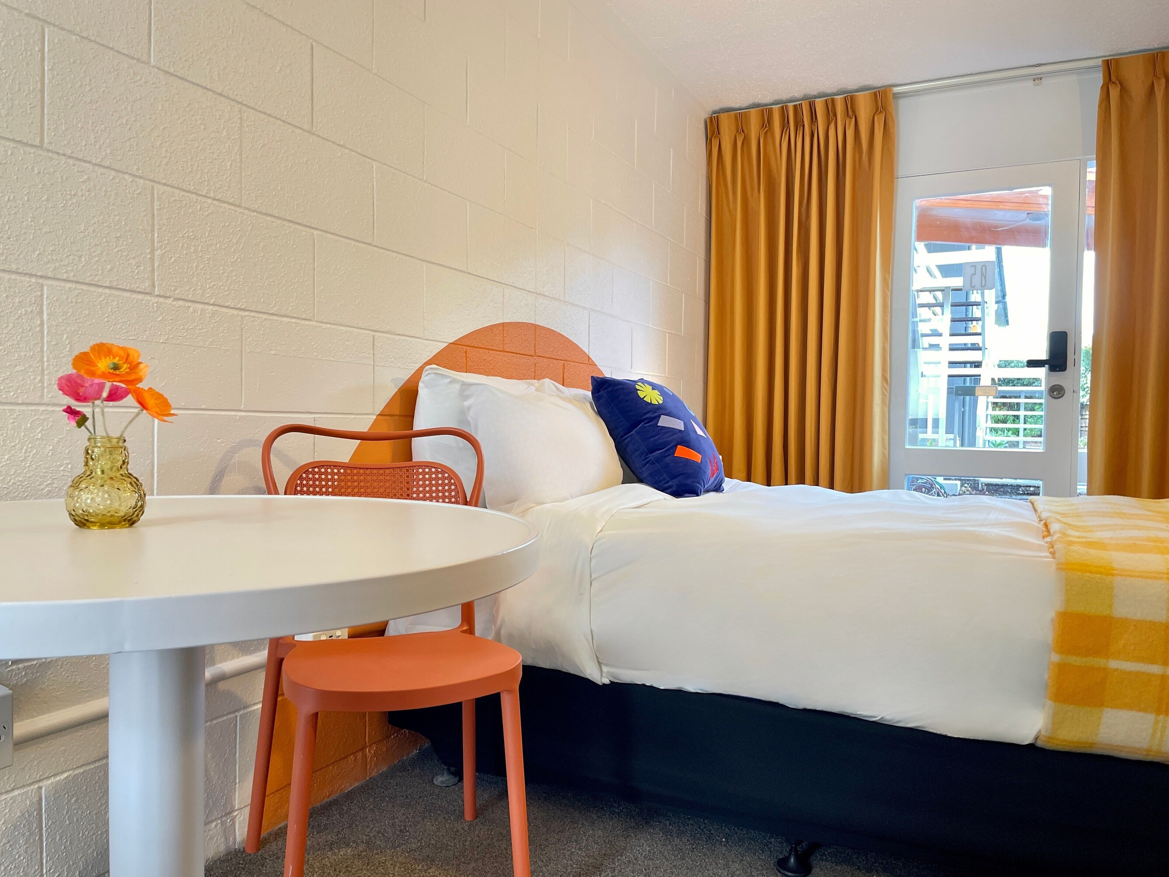 A hotel room with a bed, a table with a vase of flowers, and a chair.