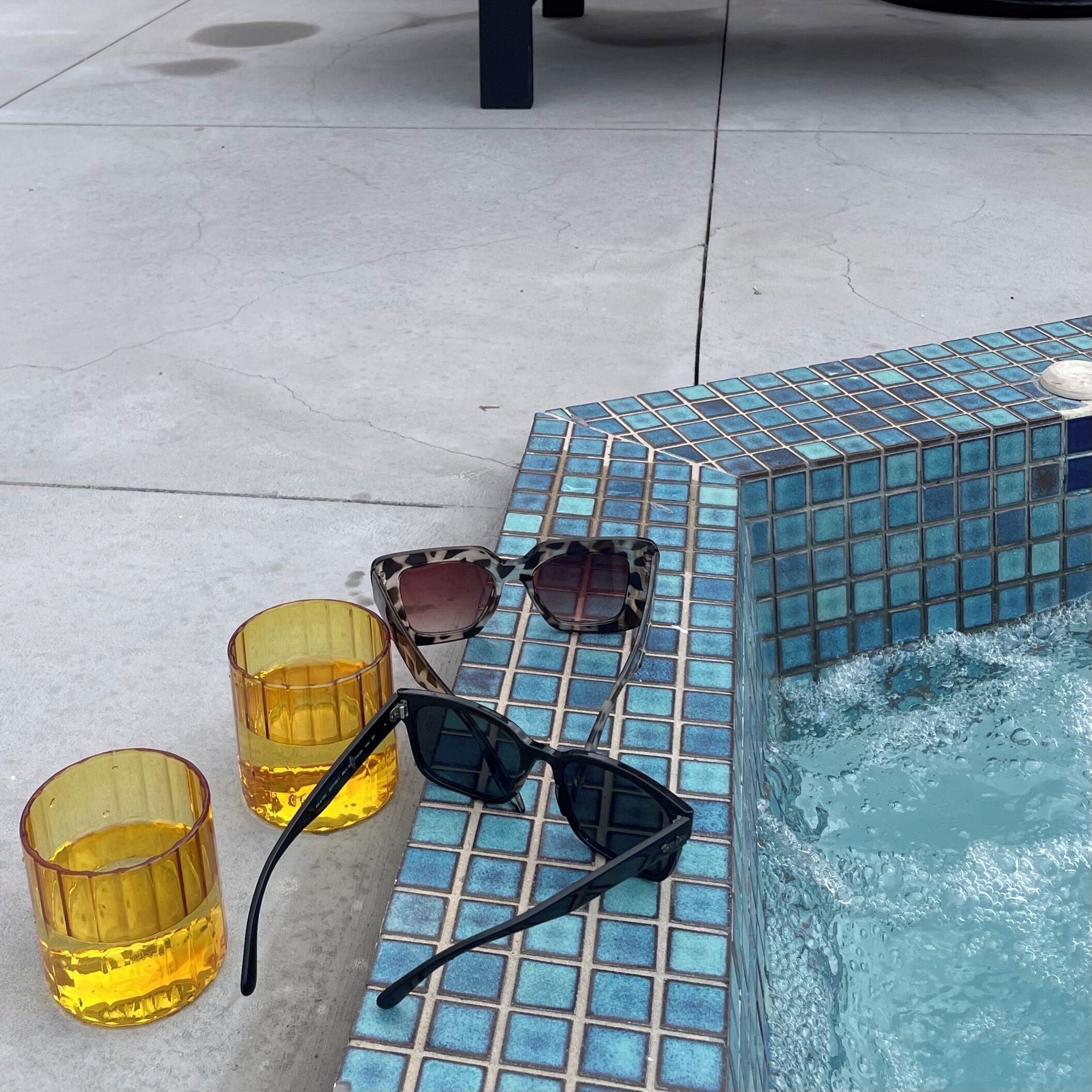 A tiled pool area with glasses and sunglasses.