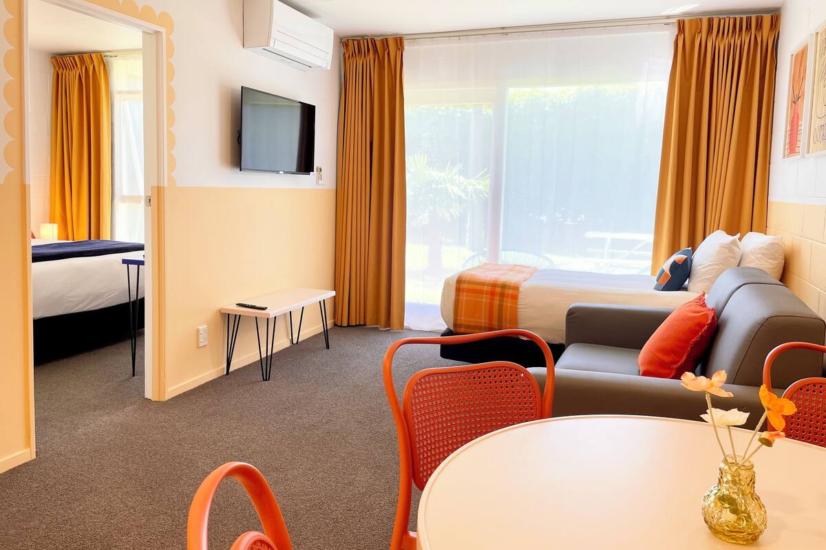 Quarto de hotel com cama, televisão, sofá, mesa de jantar e vista para o exterior.