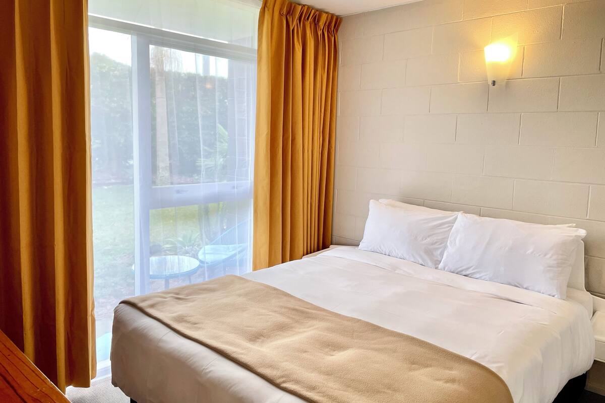 Quarto de hotel com cama, janela com cortinas, luminária na parede e vista para o exterior.