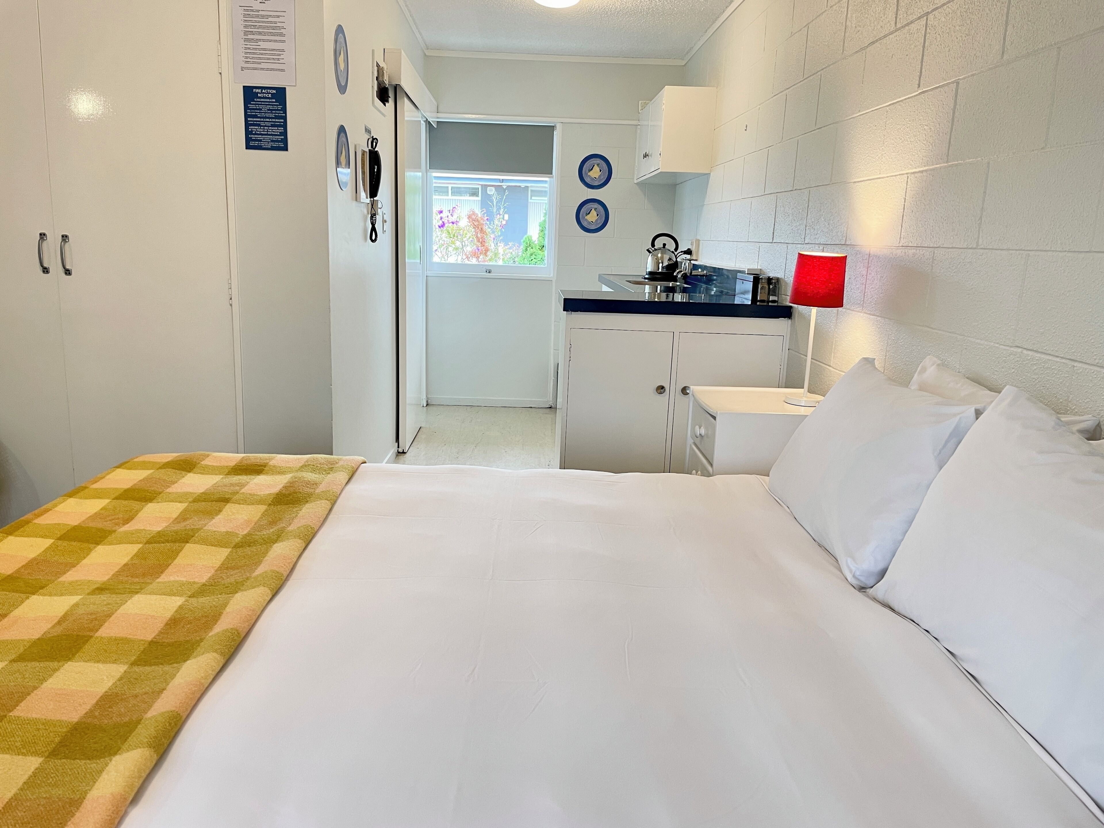 A hotel room with a bed, a small kitchenette, and a view of the outside.