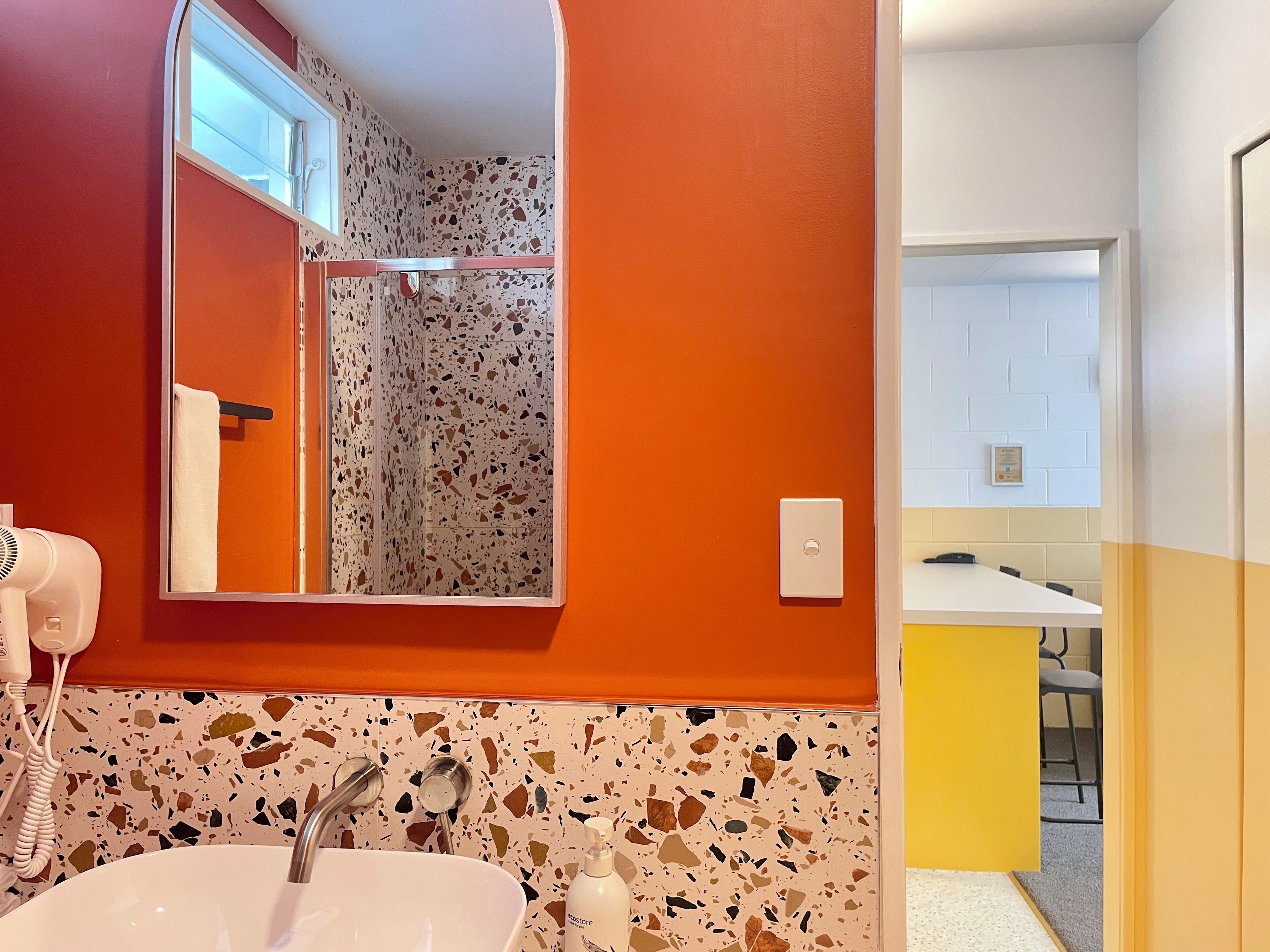 Une salle de bain avec un lavabo blanc, un sèche-cheveux, un miroir et une douche avec un sol en terrazzo.