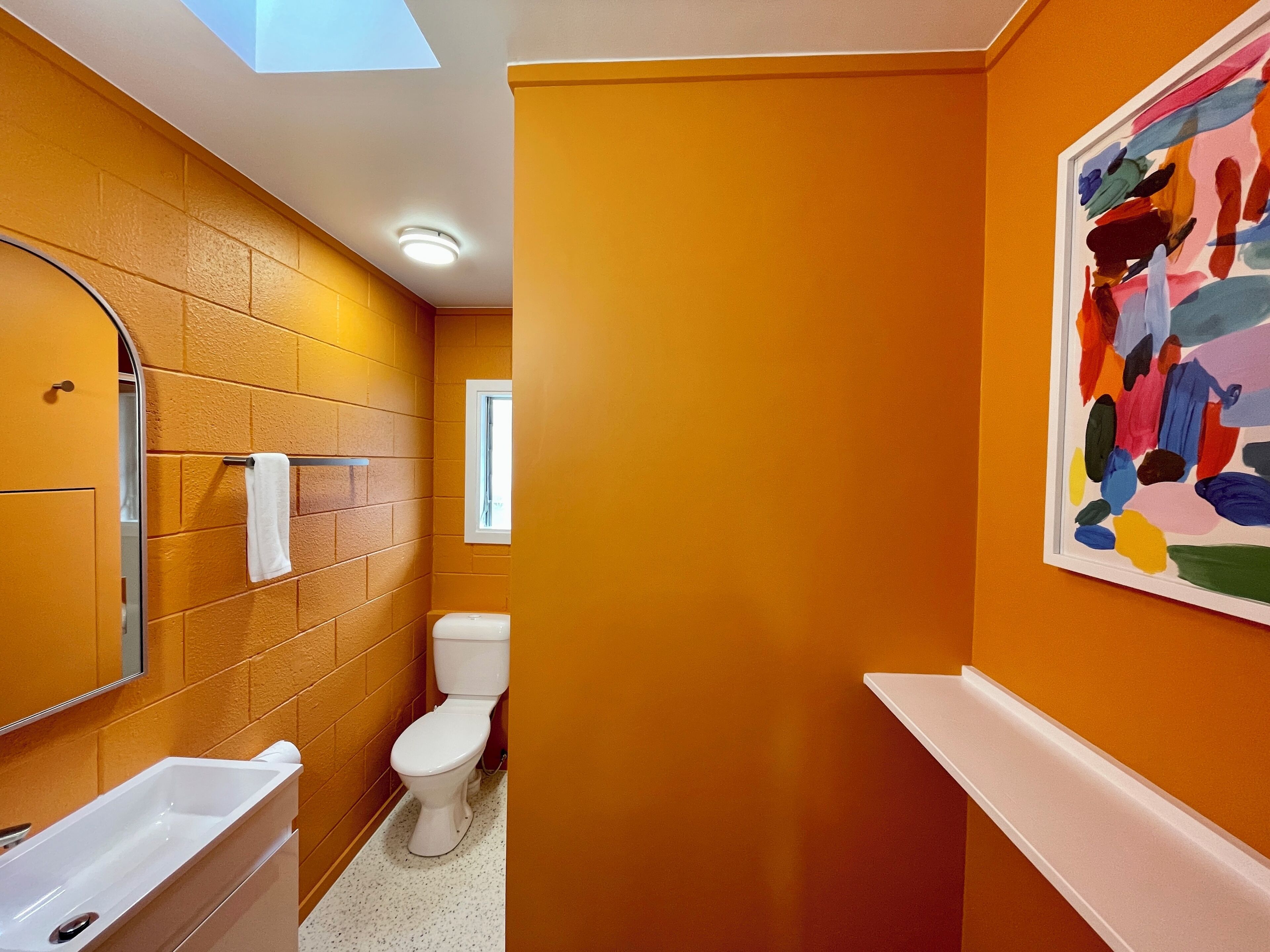 A bathroom with a white bathtub, a white toilet, and a white sink. There is a window above the toilet and a skylight above the bathtub.
