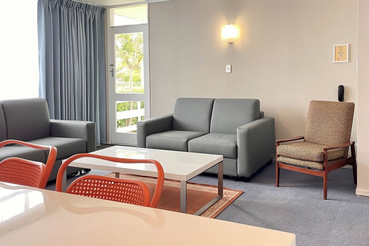 Uma sala de estar moderna com um sofá cinzento, uma poltrona estampada, uma mesa de centro branca e cadeiras laranja.