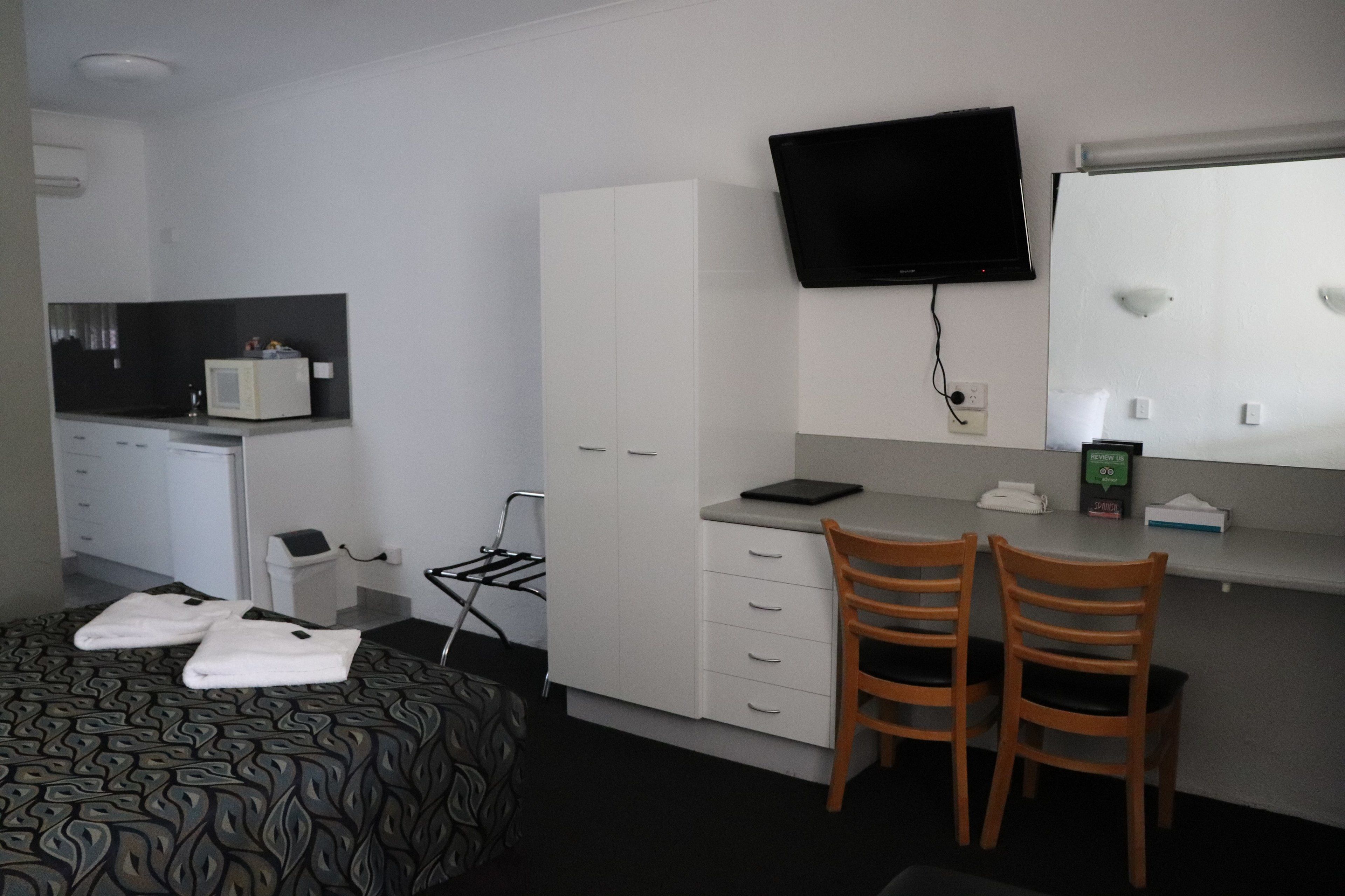 Ett hotellrum med en säng, ett skrivbord, två stolar, en tv, en mikrovågsugn och ett litet skåp.