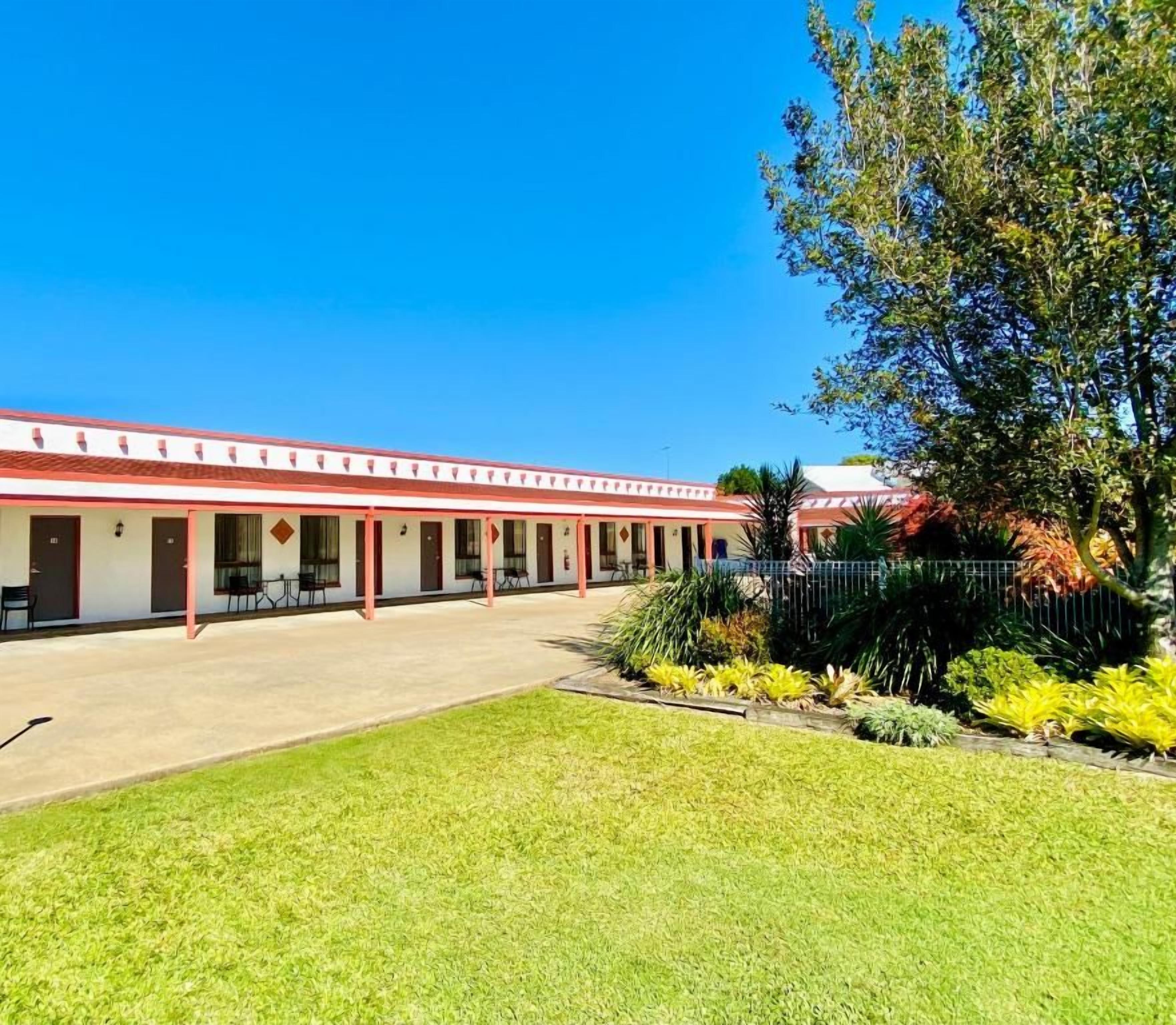 A motel with a row of rooms, a covered outdoor area, and a well-maintained lawn.