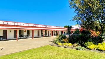 A motel with a row of rooms, a covered outdoor area, and a well-maintained lawn.