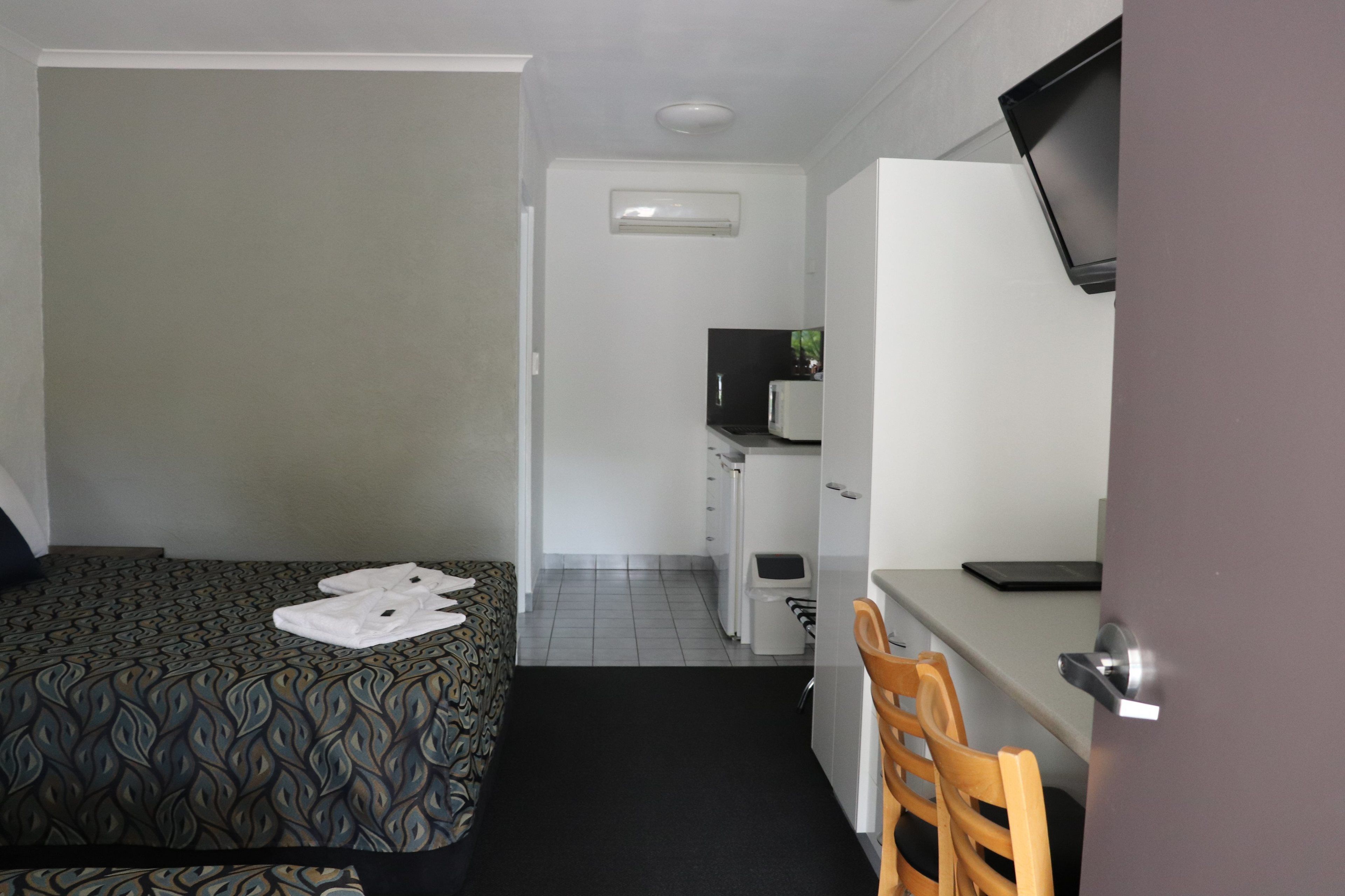 A compact hotel room with a bed, a desk, a chair, a television, and a kitchenette.