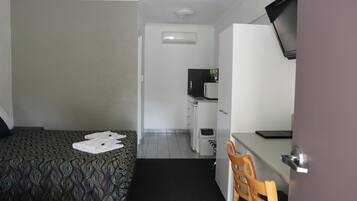 A compact hotel room with a bed, a desk, a chair, a television, and a kitchenette.