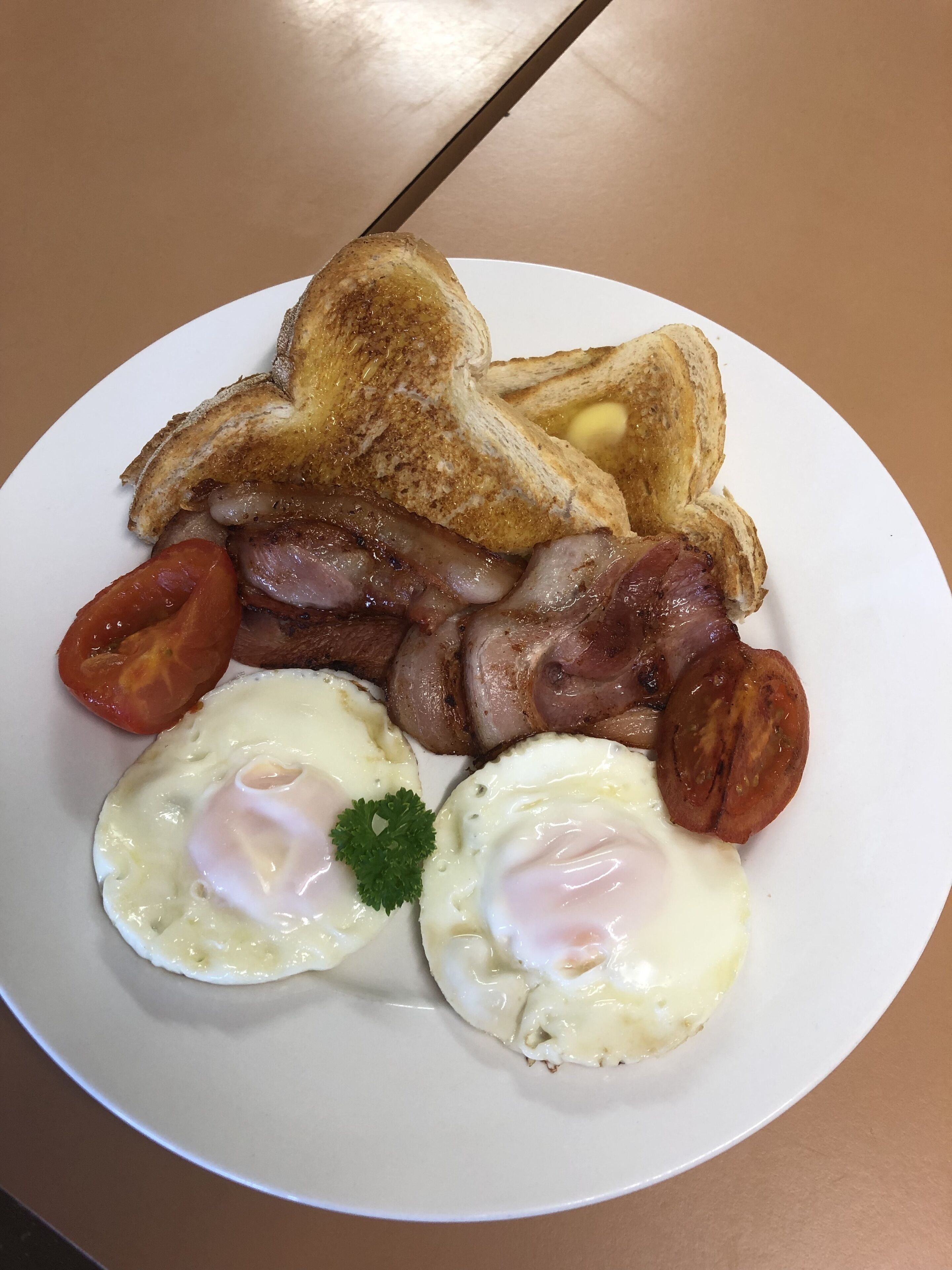 A plate of breakfast food including toast, bacon, sausages, tomatoes, and eggs.