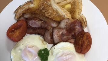 A plate of breakfast food including toast, bacon, sausages, tomatoes, and eggs.