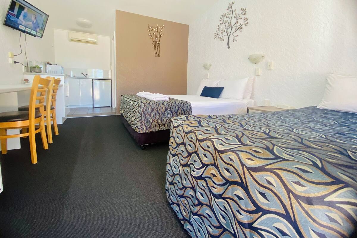 A hotel room with a bed, a desk, and a chair. There is a television mounted on the wall.