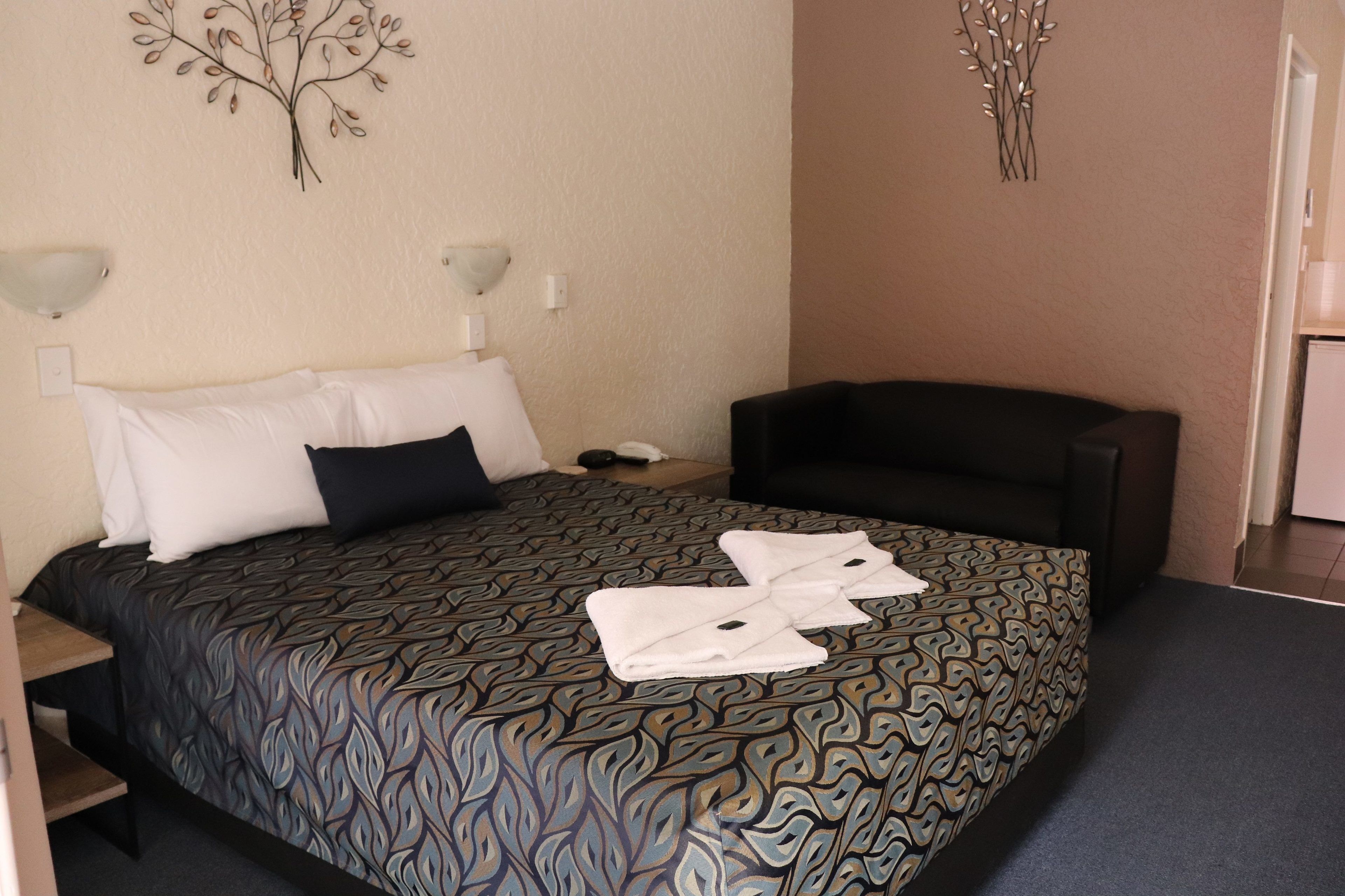 Una habitación de hotel con una colcha estampada, un sofá negro y decoración en las paredes.