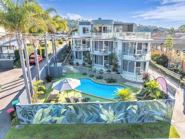 A modern hotel with a swimming pool, outdoor seating, and a tropical-themed mural.