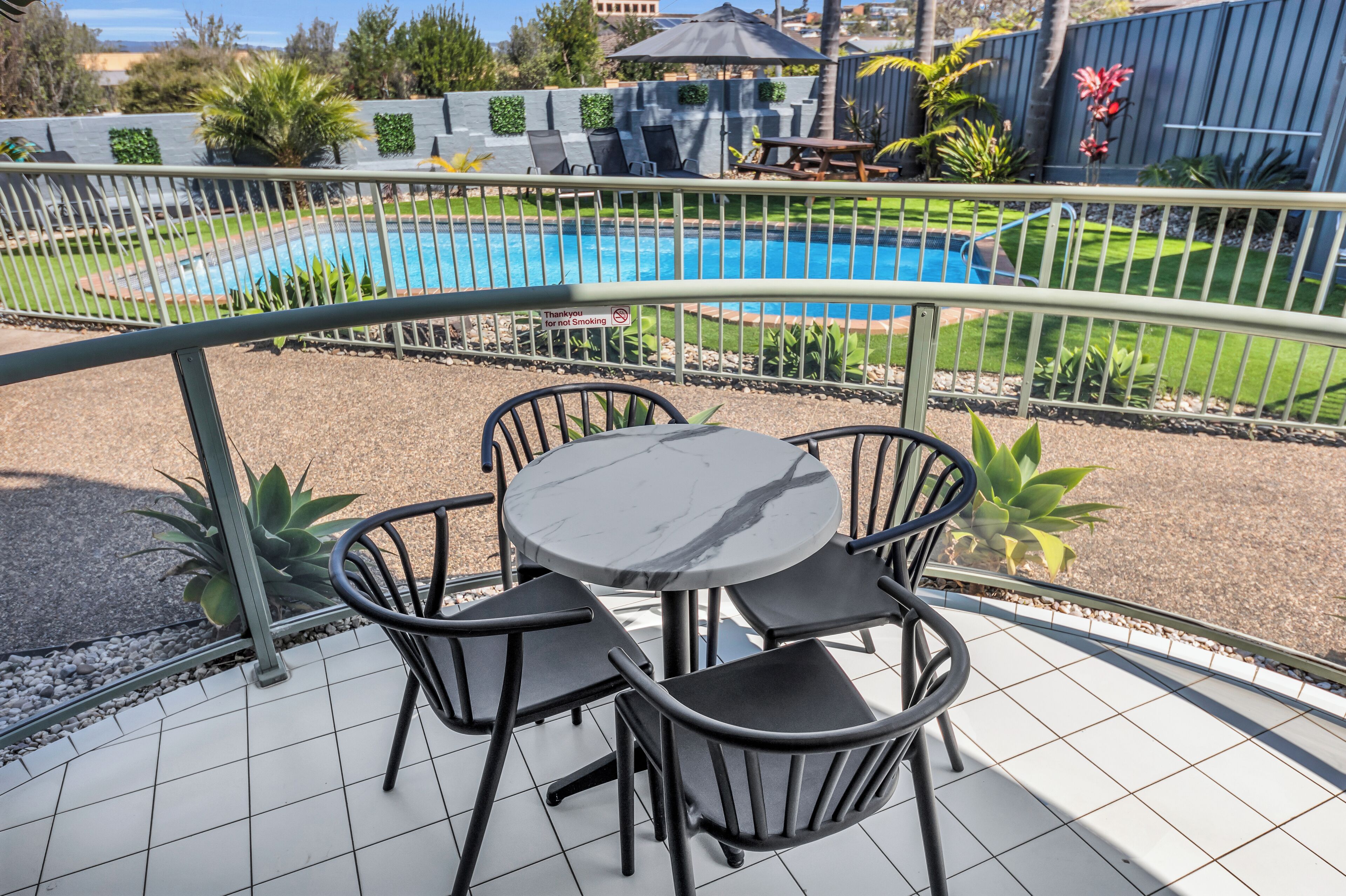 A patio with a round table and four chairs, a pool in the background, and a metal railing.